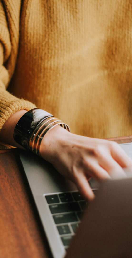 Main tenant un ordinateur portable, bracelets en bijou visibles. - Agence web Prism'